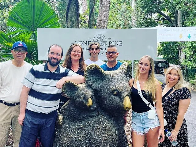 Group of people pose behind a koala sculpture at Lone Pine Koala Sanctuary.